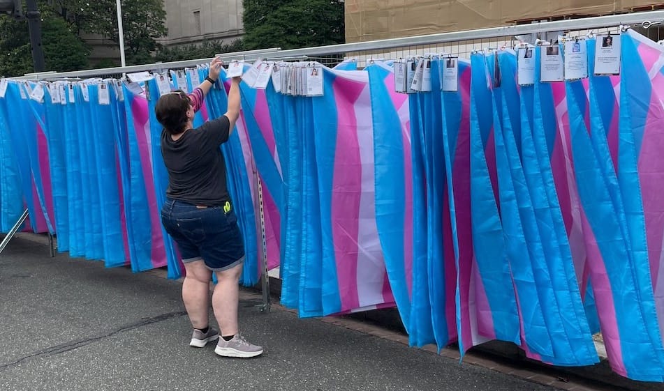 A memorial wall to remember trans people killed by violence, composed of hundreds of trans flags hanging from a coat hanger-style rack. 
